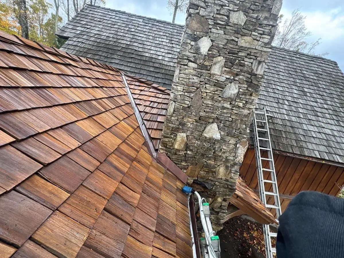Cedar shake roof half cleaned beside a stone chimney at Elk River in Banner Elk