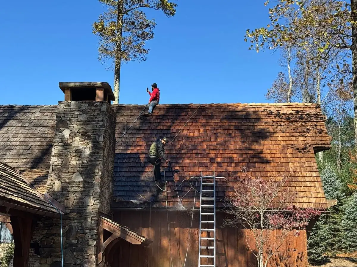 Crew cleaning a cedar shake roof beside a stone chimney