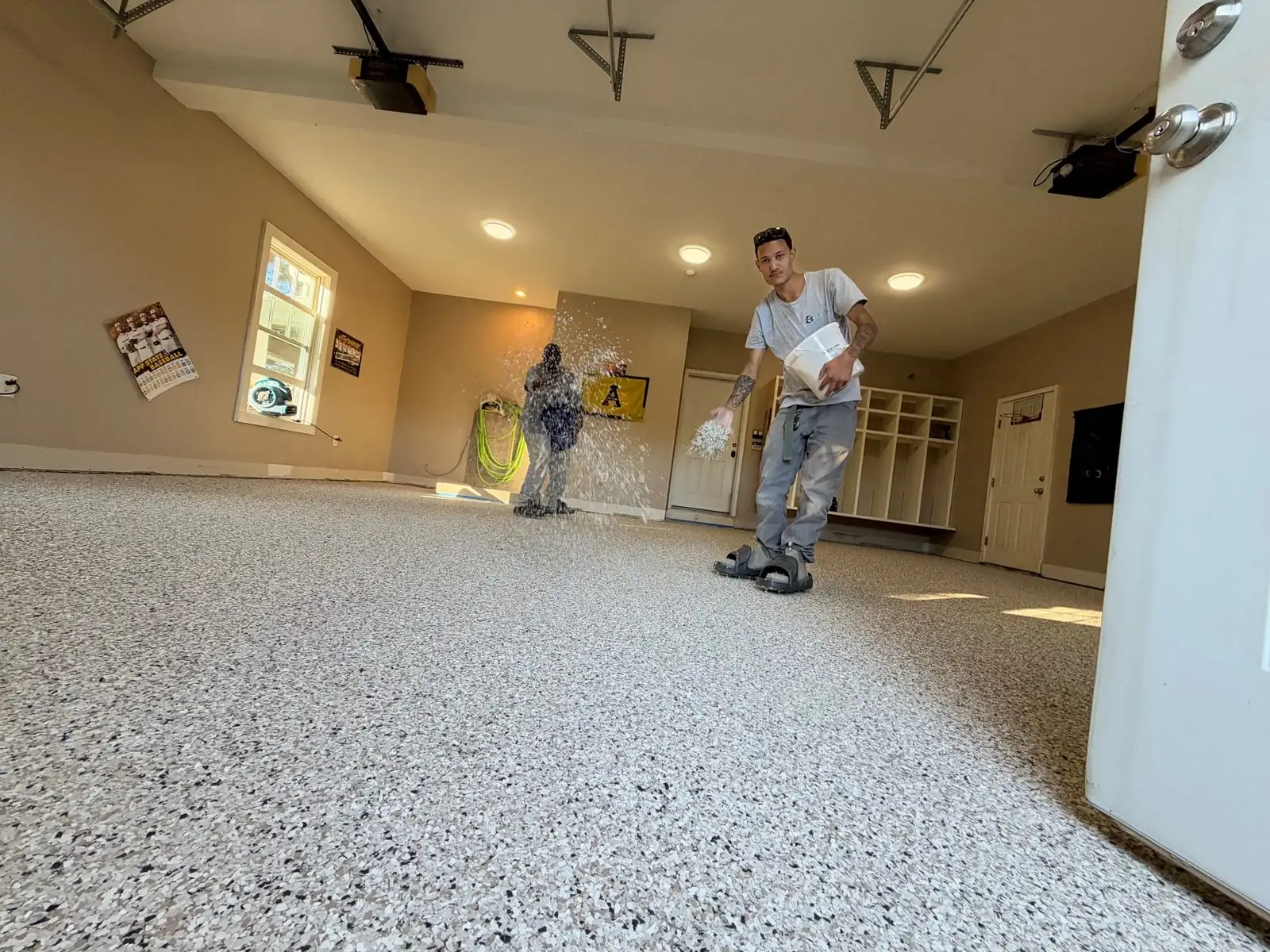 Crew broadcasting decorative flake onto a wet epoxy base in a garage in Boone