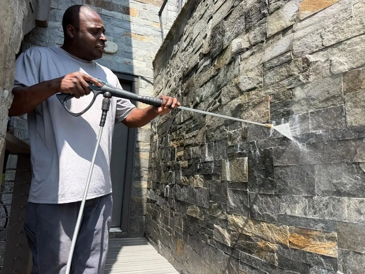 Technician pressure washing a dark stone veneer wall at Blue Ridge Mountain Club in Boone